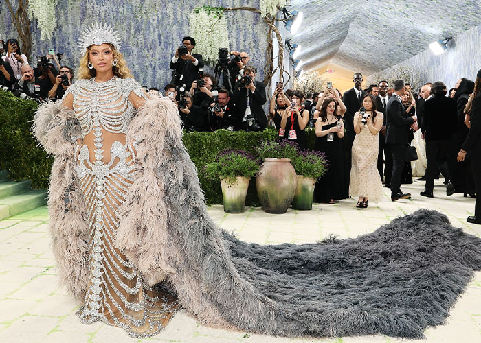 A celebrity in a skeleton-inspired feathered gown and crown at the Met Gala 2026. Worst dressed star on red carpet.