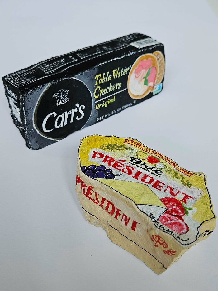 Colorful stone creations: rocks painted as a box of Carr's crackers and a wedge of President Brie cheese.