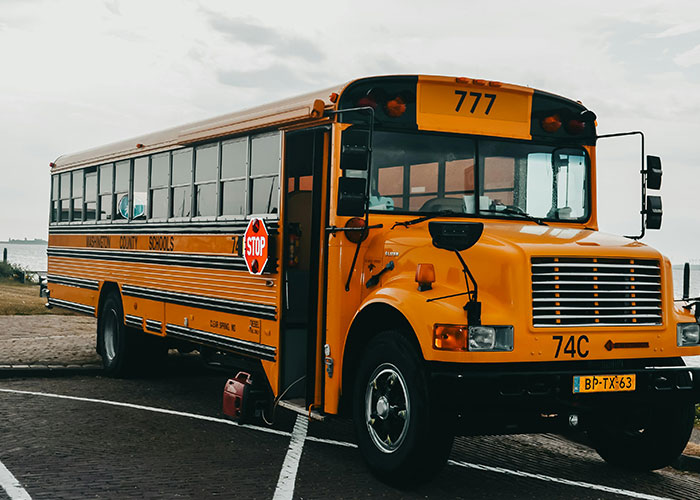 Classic yellow US school bus with a red stop sign, parked on a paved surface near water. Challenging stereotypes.