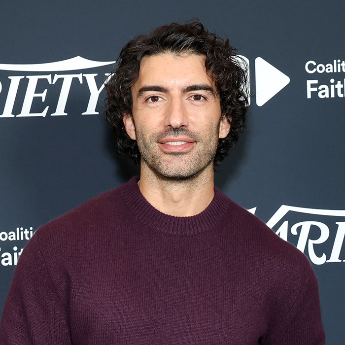 Justin Baldoni smiling, with dark curly hair and a purple sweater, against a Variety backdrop. Blake Lively and Justin Baldoni.