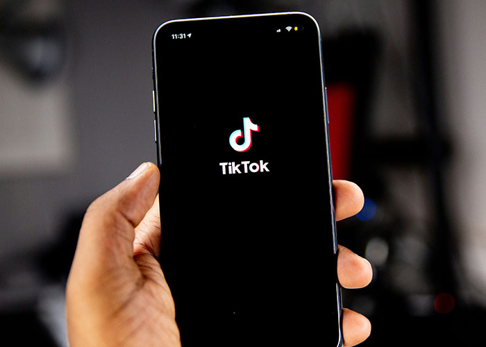 A hand holding a smartphone displaying the TikTok logo. Related to things people of low intelligence do.