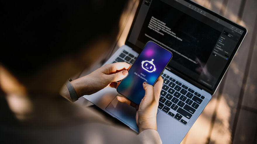 A person holds a phone displaying a chatbot, with a laptop in the background. Scientific breakthroughs changing daily life.