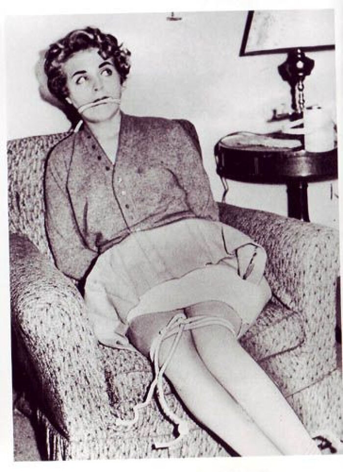 Black and white creepy photo of a woman tied up and gagged sitting in an armchair