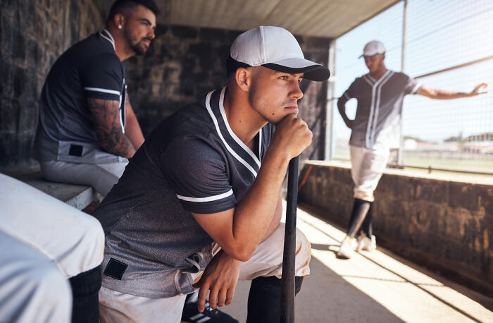 Three baseball players in a dugout; one looks pensive. The costs of being a celebrity relative can be high.