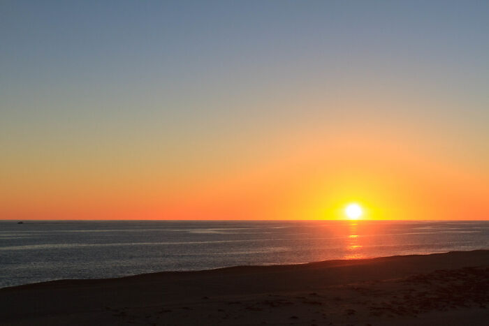 Sunset over ocean horizon with clear sky and beach foreground