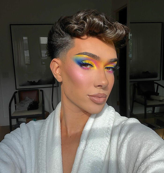 James Charles selfie with vibrant blue and yellow eye makeup in white robe