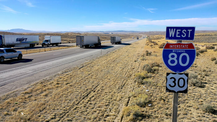 Trucks driving on Wyoming Interstate 80 with highway sign beside desert road