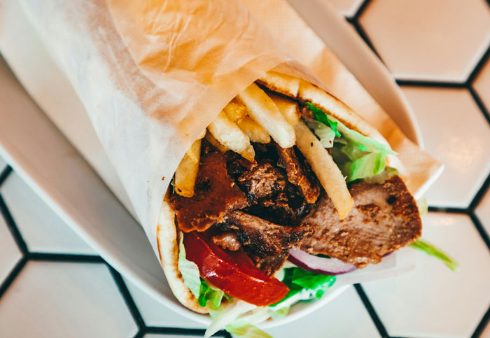 Close-up of a delicious gyros wrap filled with meat, fries, lettuce, and tomato, hinting at weirdest packages.