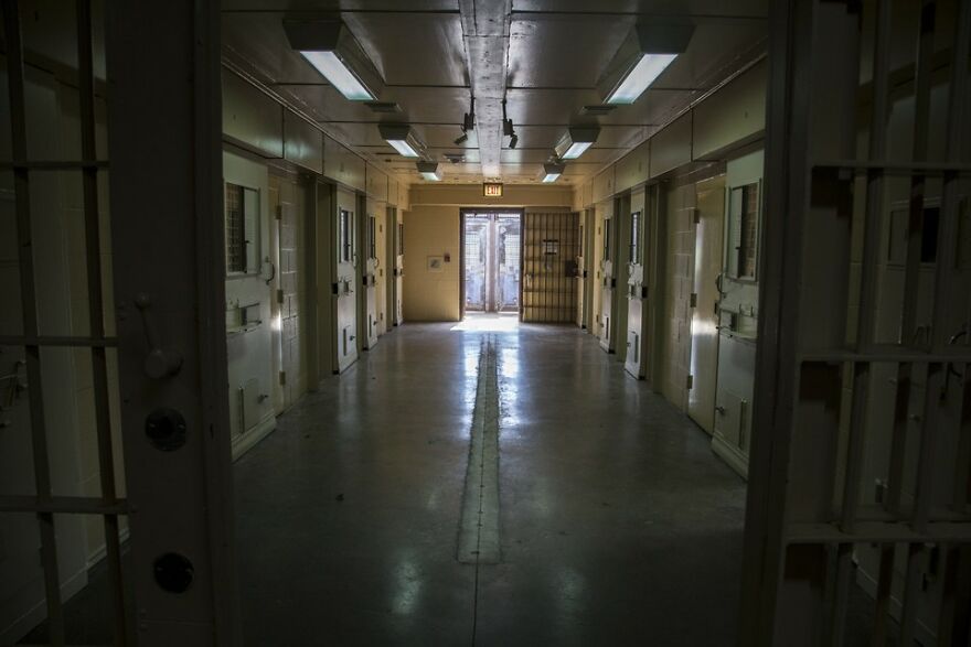 A long, dimly lit prison hallway with rows of cells, highlighting a stressful job environment.