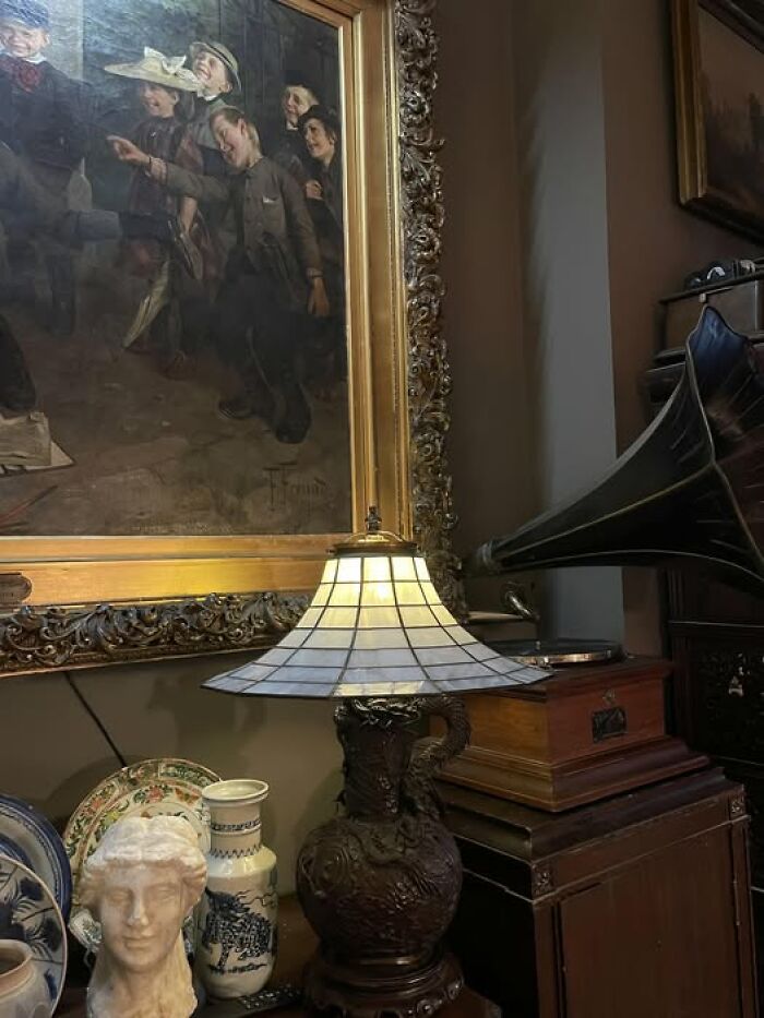 Antique vintage secondhand lamp with stained glass shade near framed painting and vase