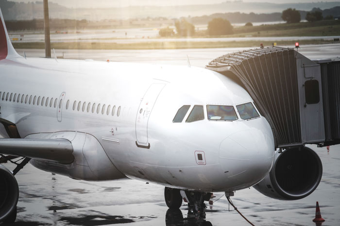 Close-up of airplane nose near airport jet bridge at sunset