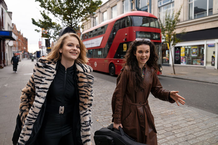 Two women walking by a red London double-decker bus