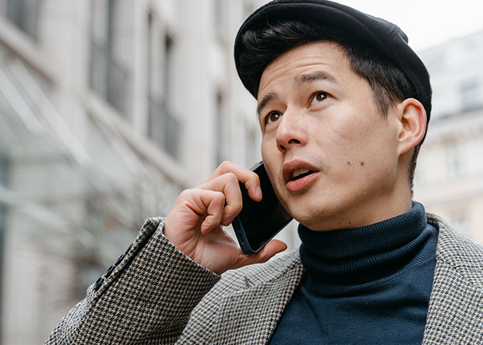 Man in beret speaking on phone outdoors with worried expression.