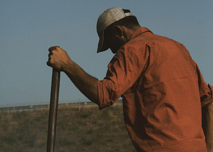 Man wearing cap holding a tool with rural background