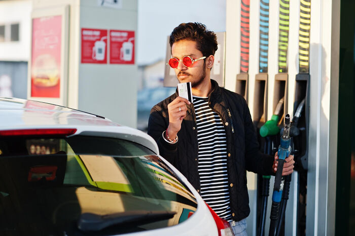 Man at gas station holding credit card and fueling car at pump