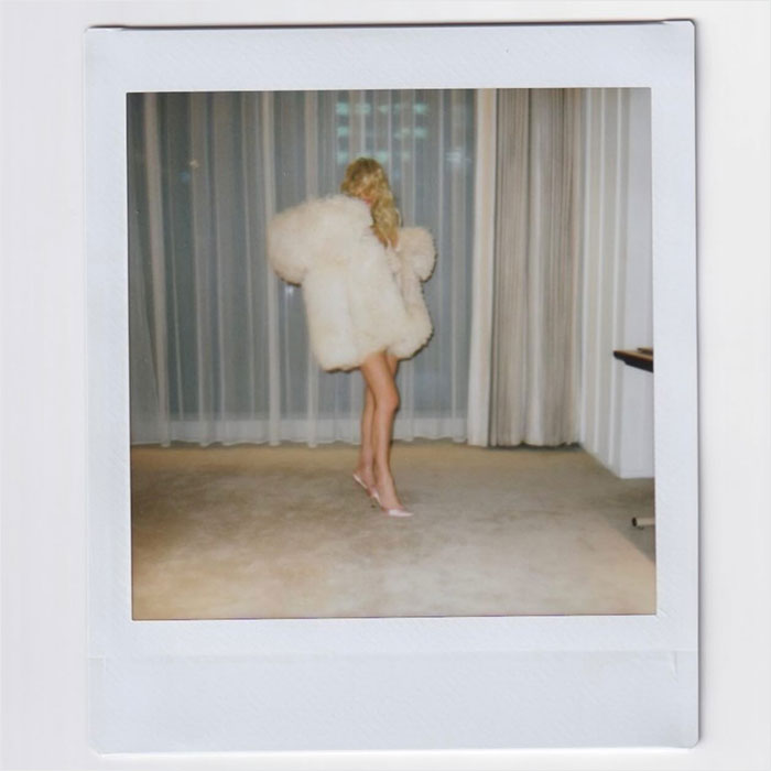 Bianca Censori com um casaco branco fofo e salto rosa, vista em uma polaroid sincera, exibindo novo cabelo e roupa transparente.