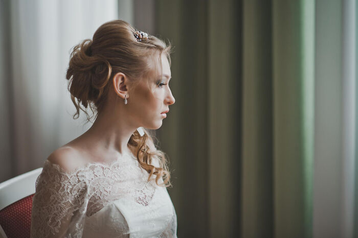 Bride in lace dress looking thoughtfully by window before wedding