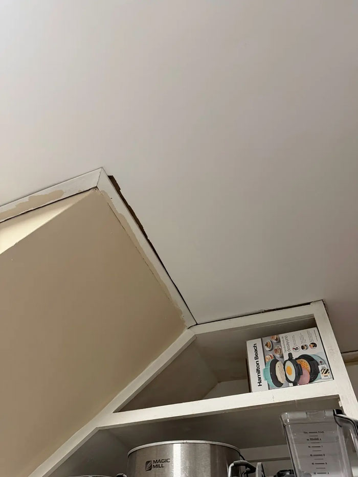 Poor contractor work: unfinished ceiling and wall corner, revealing gaps and mismatched paint near kitchen cabinets.