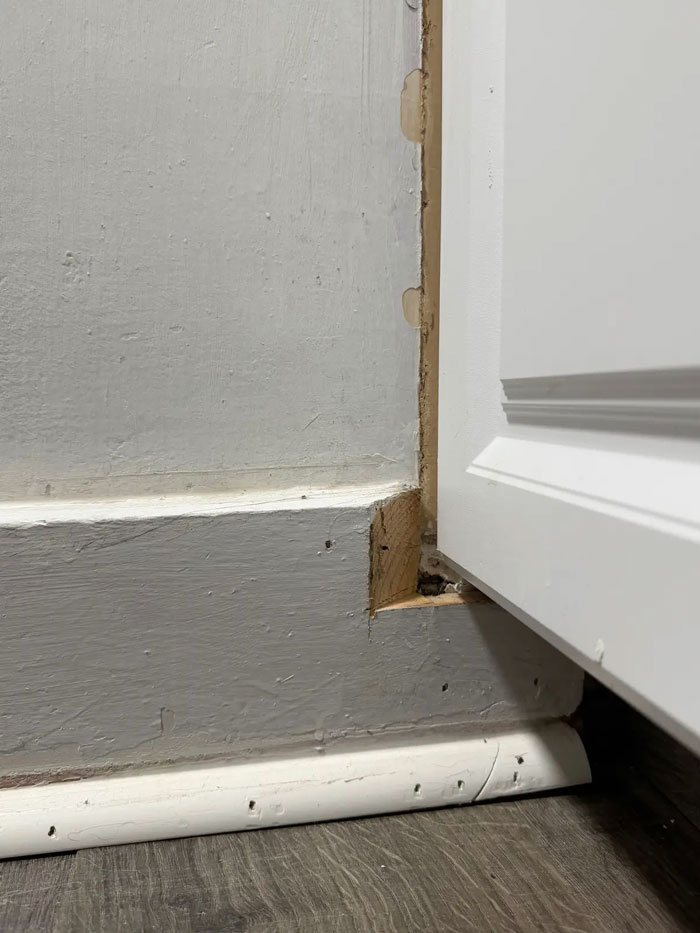 Poorly installed baseboard and trim by a contractor, showcasing visible gaps and unfinished wood near a white cabinet.