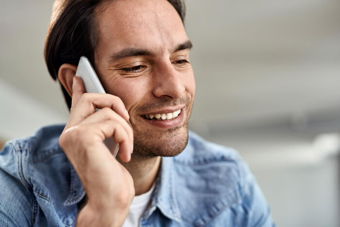 Smiling man in a denim shirt on a phone call, perhaps discussing the honest stories of celebrity relatives.