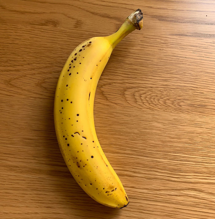 A ripe banana with brown spots on a wooden table, resembling one of the weirdest packages.