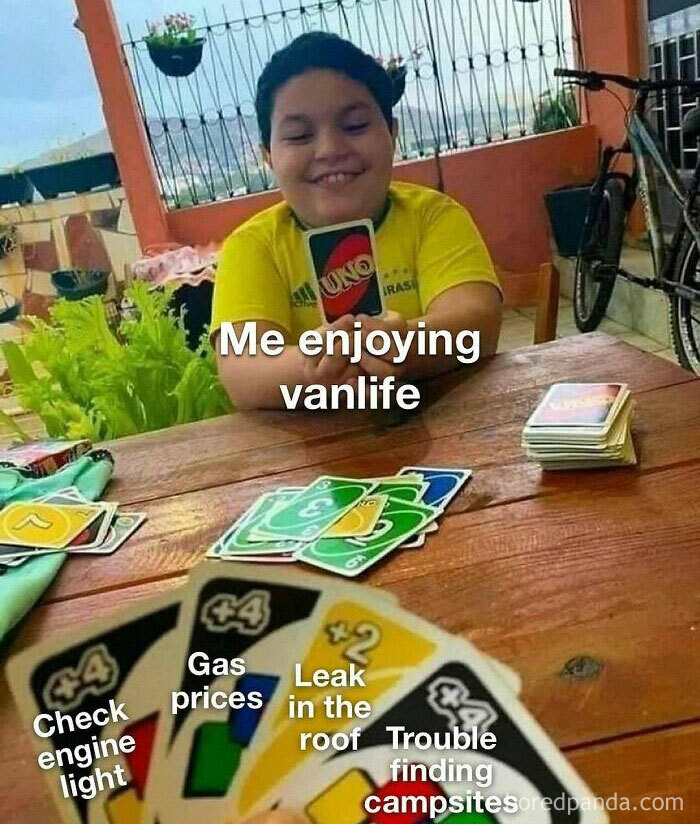 A smiling person playing Uno, holding a +4 card while other cards on the table represent the reality of living out of a van.