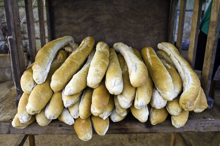 A large pile of freshly baked baguettes on a rustic wooden stand. High-carb foods impact diets in many countries.