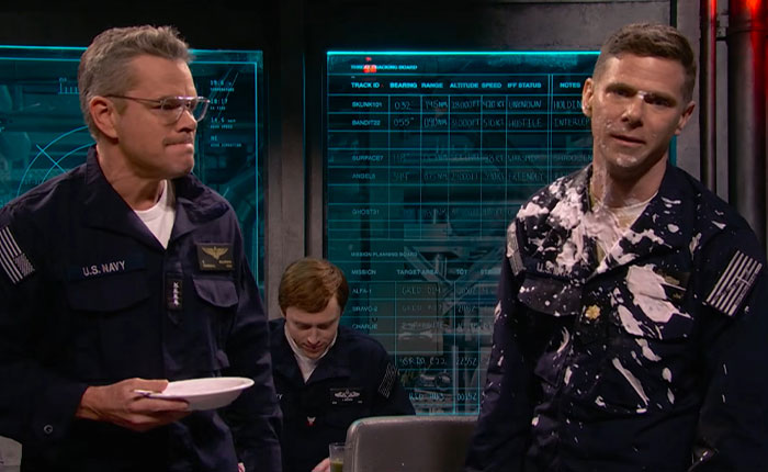 Matt Damon in a US Navy uniform holding a bowl, next to a man covered in white goo, a gross SNL sketch.