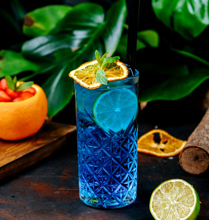 Blue artisinal cocktail with garnish on rustic wooden table