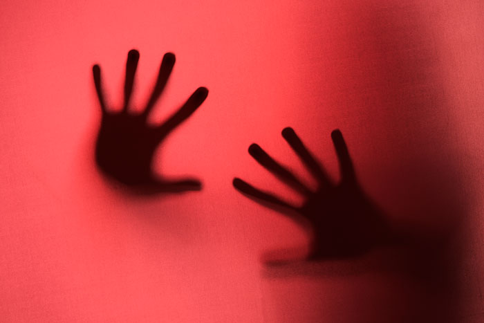 Shadowy hands on red background depicting anxiety and mental health struggles