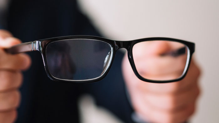 Person holding black framed eyeglasses close up