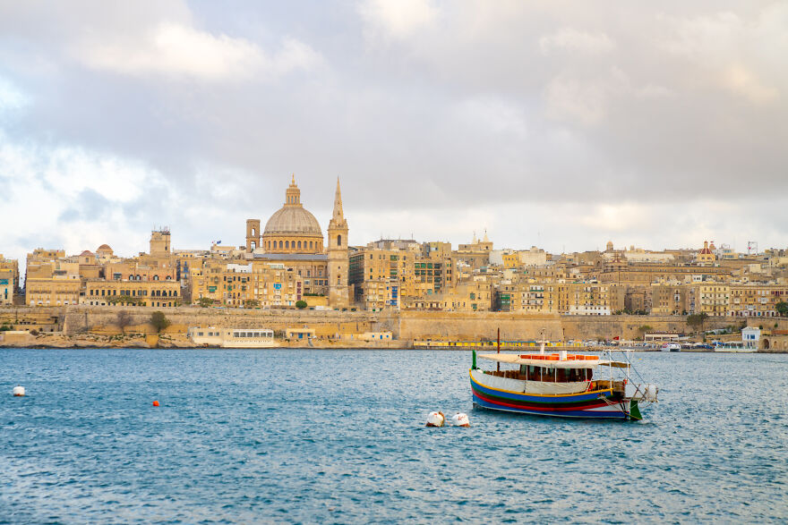 Historic city skyline with a colorful boat in water, showing one of the smallest countries
