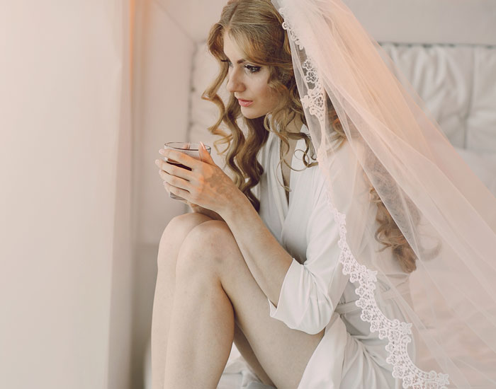 Bride in veil holding cup looking pensive before wedding day