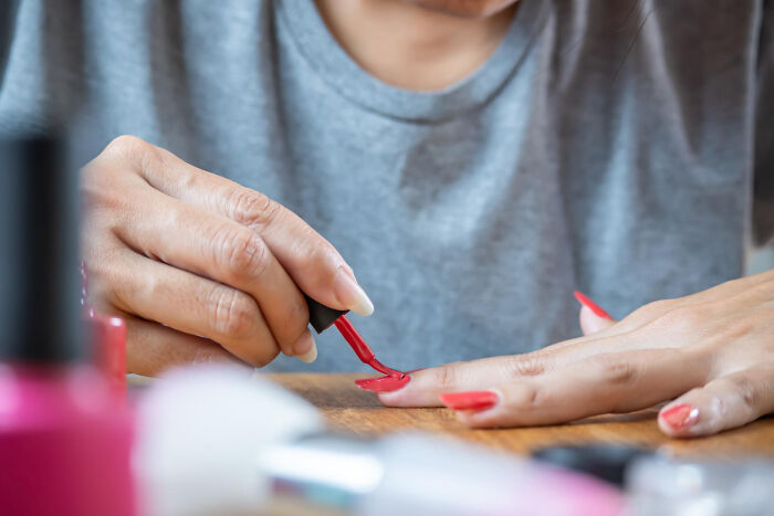 A woman in a grey shirt applying red nail polish, surrounded by other beauty products. Reflects the fun of engagement stories.