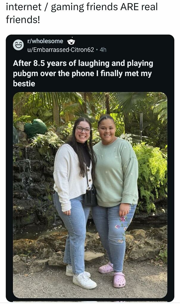 Two smiling friends, having met in person after 8.5 years of online gaming, standing in front of a waterfall and lush greenery. This positive post might make your day!