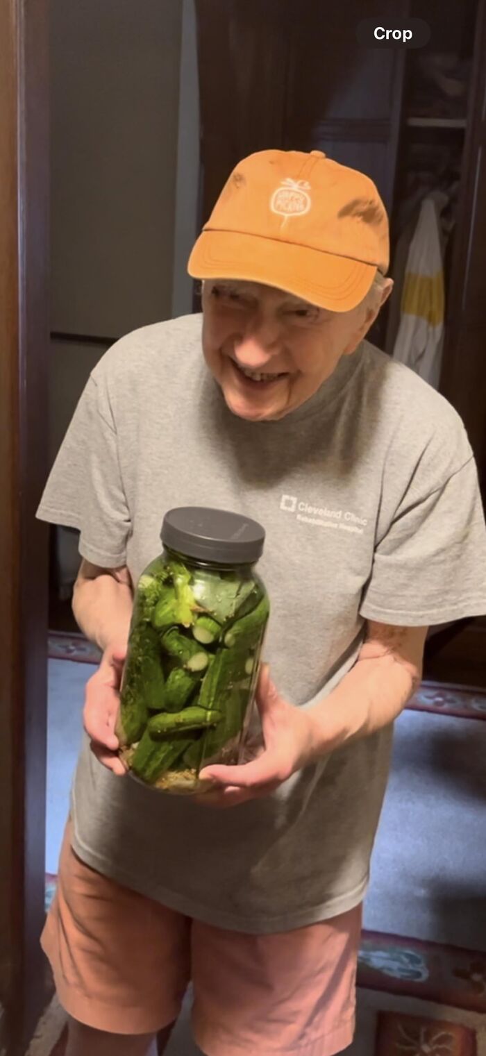 Elderly man joyful holding jar of homemade pickles in kitchen