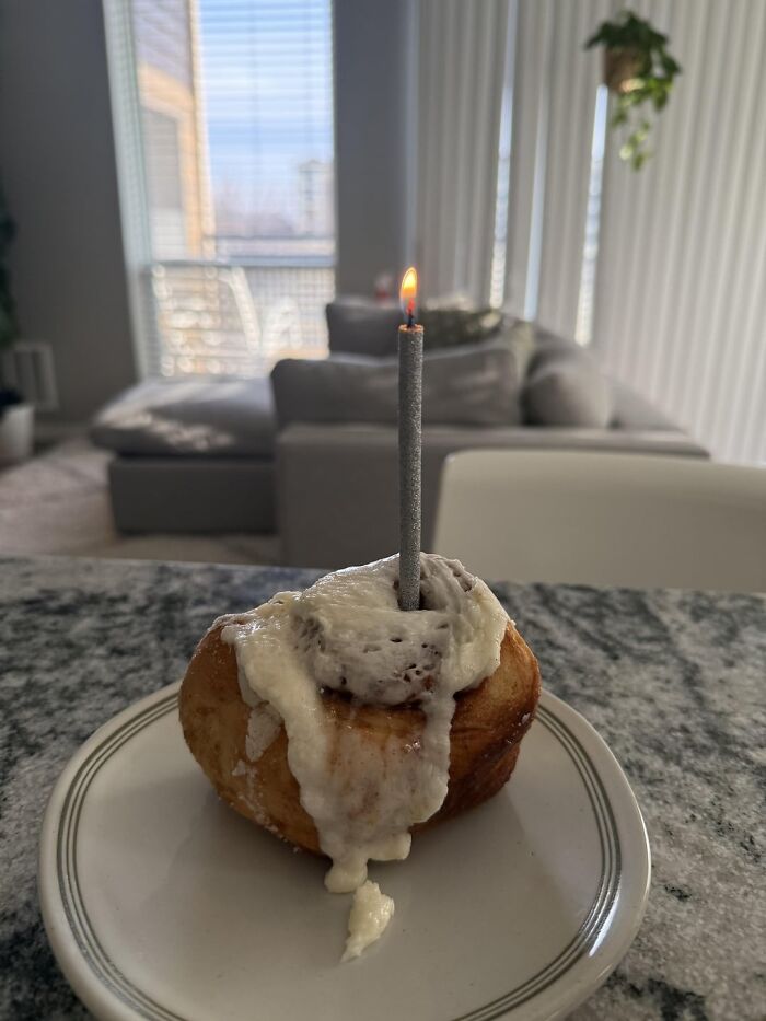 Cinnamon roll with lit candle on plate in bright cozy living room