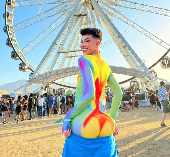 James Charles smiling in colorful bodysuit in front of large Ferris wheel