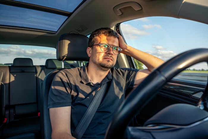Man sitting in car looking distracted while driving wearing glasses