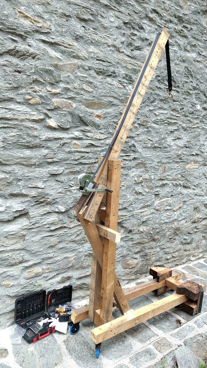 A DIY wooden crane used as a clever solution for lifting, standing against a stone wall with tools nearby.