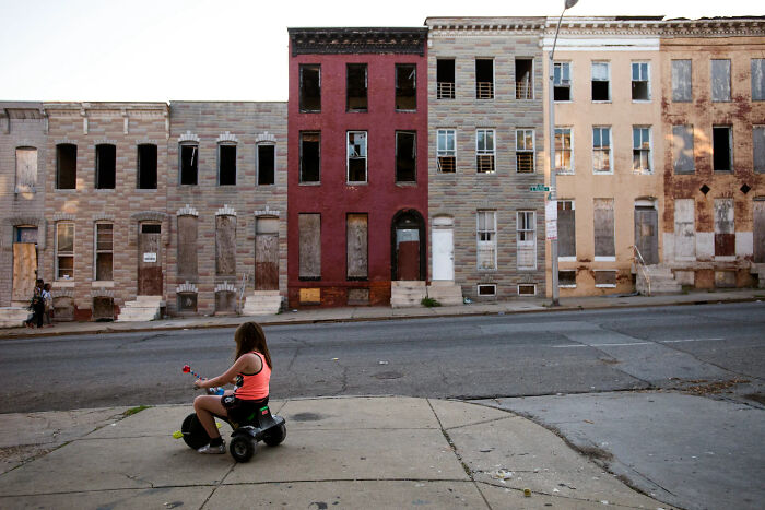 Urban hell abandoned row houses with boarded-up windows and child on toy vehicle