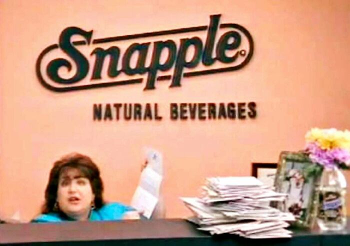 A woman at a reception desk with the Snapple Natural Beverages logo, a throwback meme for 90s kids, depicting a vintage office.