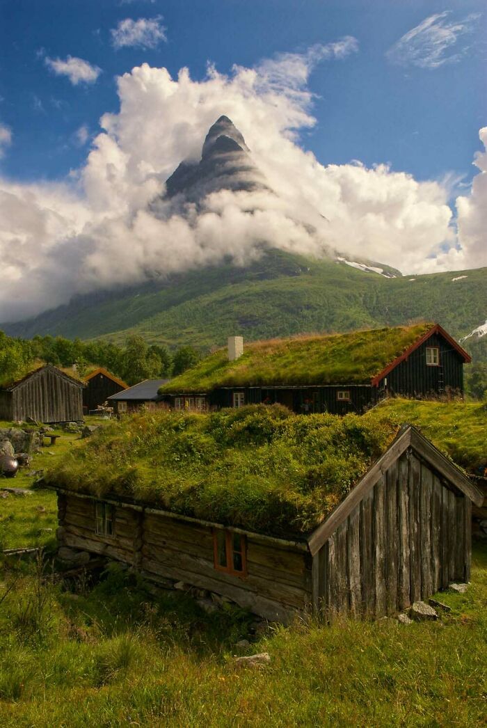 Traditional houses with grass roofs and a mountain peak in the clouds, an interesting post.