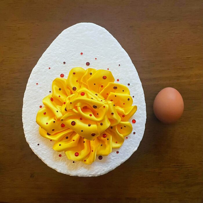 A handmade egg yolk art piece made of yellow ribbons and red/black dots next to a brown egg.