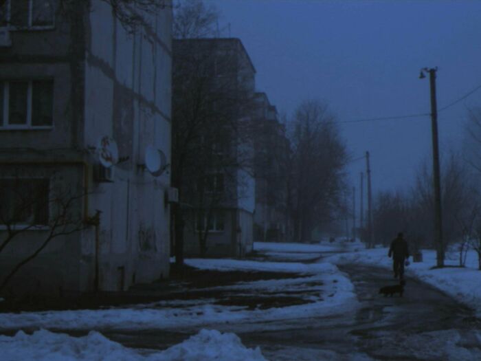 Urban hell dimly lit street with snow and solitary person walking a dog