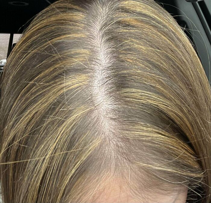 Close-up of a person's part, revealing significant root growth on blonde hair, a common beauty disaster.