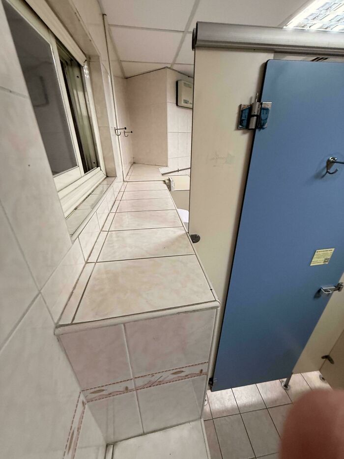 Narrow tiled ledge along bathroom stalls limiting space and access in public bathroom