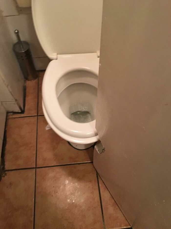 Toilet cramped behind a door that obstructs access in a tiny bathroom