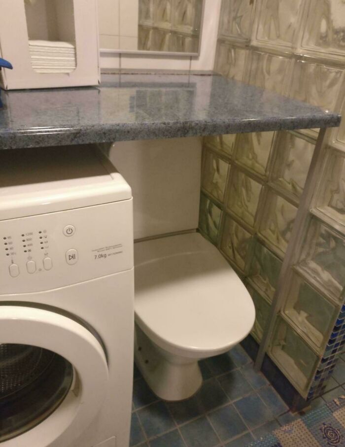 Small bathroom with toilet placed under a countertop beside a washing machine