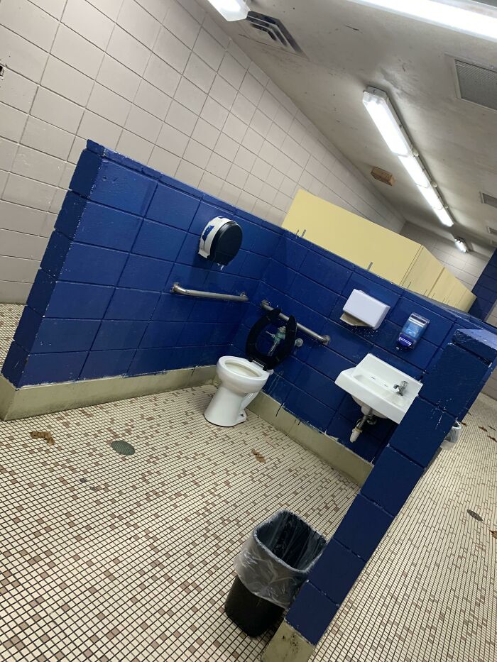 Handicap accessible toilet and sink in a poorly designed large blue tiled bathroom